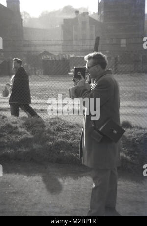 1960, historische, eine lokale Nachrichten Reporter mit einem 8-mm-cine Film oder Film Kamera außerhalb Norwich Football Club vor einem Spiel, Norwich, England, UK. Stockfoto