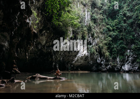 Mann hockt auf einem Felsen im Meer Höhle in Krabi, Thailand Stockfoto