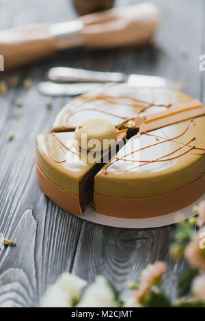 Bäckerei mit ungewöhnlich gelbe Mousse Torte mit Mandel-Dacquoise, Himbeer-Confit, knusprige Schicht mit karamellisierten Haselnüssen und Himbeere Pulver, Mousse, basierend auf Bitterschokolade serviert auf Holztisch Stockfoto