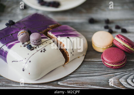 Details einer Hochzeit oder einem Geburtstag lila Kuchen, im Studio auf Holz- Hintergrund. Lila kleine Macarons als Dekoration. Stockfoto