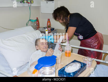 Ältere Patienten in den 90er Jahren mit der Diagnose Krebs lesen Mittagsmenü in NHS-Krankenhaus in England als weiblichen Verwandten ihr Haar Kämme Stockfoto