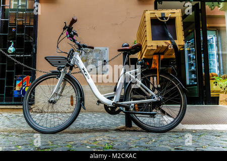 Weißes Fahrrad mit Holzlieferkorb, für die Lieferung von Lebensmitteln Kurierdienst, geparkt und vor einem Geschäft verschlossen. Rom, Italien, Europa, Europäische Union, EU Stockfoto