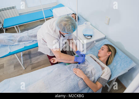 Krankenschwester macht eine Injektion mit einer Frau am OP-Tisch am Klinikum Vorbereitung Narkose medizinische Arztpraxis Konzept liegen. Stockfoto