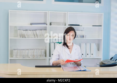Die jungen praktizierenden Arzt an der Klinik Rezeption arbeiten, ist sie Entgegennehmen von Anrufen und Planen von Terminen Stockfoto