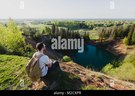 Junger Mann Tourist mit Rucksack stehen am Rande des wunderschönen Canyon und siegreich Hände erhoben. Männliche Wanderer bis Berg und Arme ausstreckten, oben. Sicht nach hinten zurück. Stockfoto