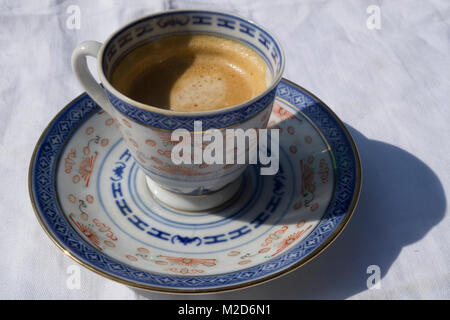 Nahaufnahme von frisch gebrühtem Espresso in einer antiken porzellanschale und Untertasse auf einer weißen Tischdecke im Freien in der Sonne Stockfoto