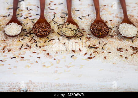 Fünf Löffel mit verschiedenen Sorten Reis auf einem alten Holz- Hintergrund. Zutaten für eine gesunde Ernährung. Stockfoto