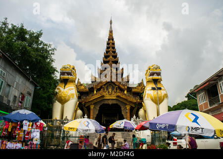 Eingang zur Shwedagon Pagode, mit Paar gelbe Chinthe Lion-wie Statuen gurading und Schutz der Pagode, Sonnenschirme in Street Market Yangon, Myanmar Stockfoto