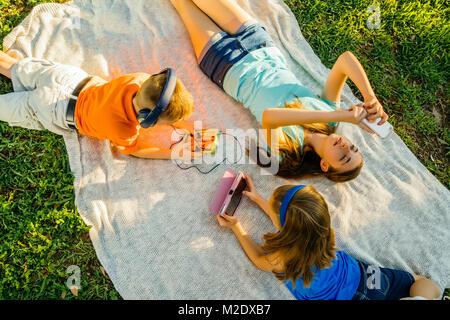 Kaukasische Bruder und Schwestern Verlegung auf Decke im Park mit Technologie Stockfoto