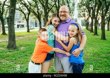 Portrait der kaukasischen Jungen und Mädchen umarmt Vater im Park Stockfoto