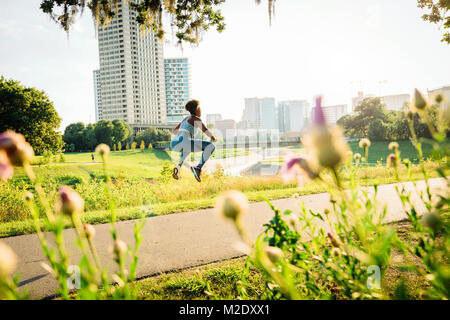 Gemischte Rasse Frau springen auf Pfad im Park jenseits Wildblumen Stockfoto