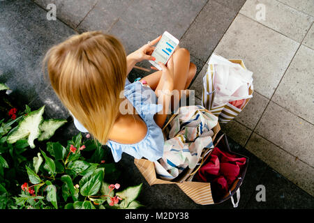 Hohe Betrachtungswinkel der kaukasischen Frau mit Einkaufstüten SMS auf Handy Stockfoto