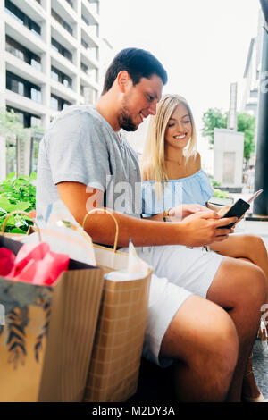 Kaukasische Paar mit einkaufstaschen Sms auf Handys Stockfoto