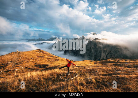 Junger Mann Wanderer in rote Jacke steht zurück zu Kamera wie fliegende Vogel oder ein Flugzeug auf einem Felsen in den Bergen Dolomiten und schaut auf das Tal, Italien, Stockfoto