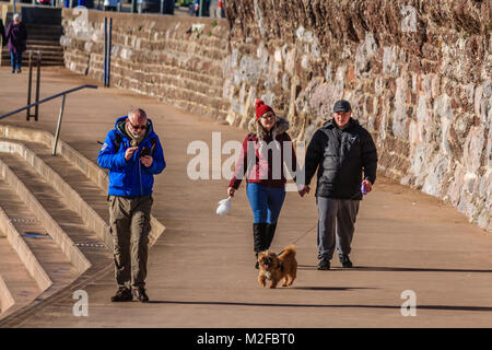 Menschen zu Fuß entlang der Promenade von Torre Strand bei Flut im Februar Sonnenschein. Nur 2 Grad C, aber viel der Leute aus trotzen der kalten aber sonnigen Morgen bei Torquay, Torbay, Devon, Großbritannien. Februar 2018. Stockfoto