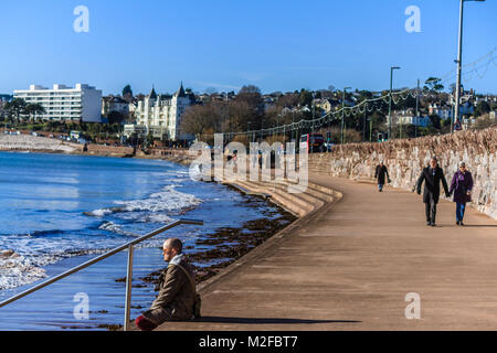 Menschen zu Fuß entlang der Promenade von Torre Strand bei Flut im Februar Sonnenschein. Nur 2 Grad C, aber viel der Leute aus trotzen der kalten aber sonnigen Morgen bei Torquay, Torbay, Devon, Großbritannien. Februar 2018. Stockfoto