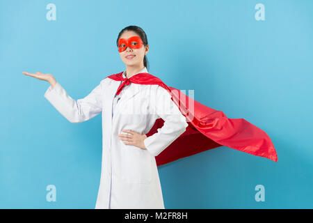 Gerne professionelle Frau Superhelden Arzt stehen in blauer Hintergrund und Präsentation Geste Gesicht in die Kamera lächelt. Stockfoto