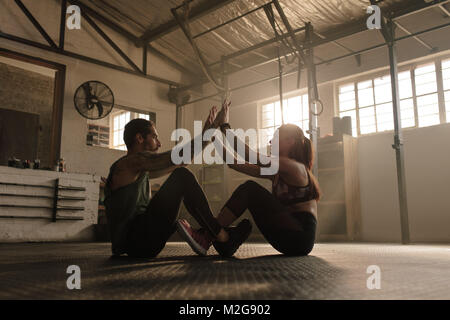 Paar zusammen trainieren im Fitnessstudio. Passen Mann und Frau sitzt auf dem Boden und dabei eine hohe fünf während eines Workout Routine. Stockfoto