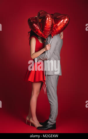 Paare, die Gesichter mit Bündel von Ballons auf Rot Stockfoto