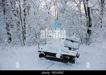 Schneemann sitzt auf einer Bank im Wald im Winter, viel Schnee, Bäume im Schnee Stockfoto