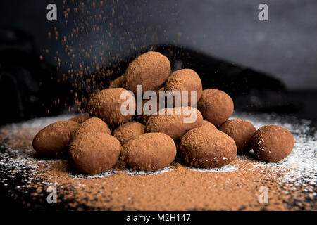 Bonbons Mandeln, umhüllt mit Schokolade Kakao einfügen auf dunklen schwarzen Hintergrund. Kakaopulver strewing auf Süßigkeiten. Stockfoto