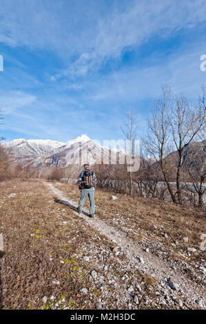 Mann Wanderer mit Rucksack und Pole zu Fuß auf den Weg über den Fluss Ufer in Richtung Berge. Stockfoto