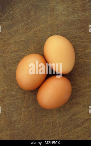Drei braun huhn eier liegen auf Zerkratzt braun Schneidebrett Stockfoto