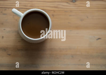 Kleine weiße Tasse mit Kaffee, stehend auf einem hölzernen Tisch gefüllt Stockfoto