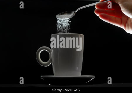 Tasse Tee und gießen Zucker Löffel auf schwarzem Hintergrund Stockfoto