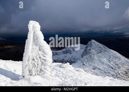 Eisige markierungsstein am oberen Watkin Pfad auf Mt Snowdon mit Y Lliwedd über im Winter Schnee in den Bergen von Snowdonia National Park. Gwynedd, Wales, Großbritannien Stockfoto