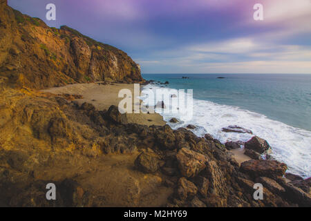 Der abgeschiedenen Pirate Cove Strand bei Sonnenuntergang mit einem bunten Himmel und Meer Wasser fließt, um Felsformationen, Point Dume, Malibu, Kalifornien Stockfoto