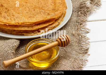 Pfannkuchen auf einer weißen Platte. Frische Honig in einem Glas. Holzlöffel für Honig. Nachtisch. Gesundes Frühstück. Die Tabelle wurde in Sackleinen abgedeckt. Stockfoto