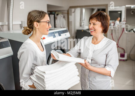Senior washwoman mit jungen Assistenten in der Wäscherei Stockfoto