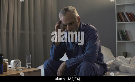 Schlaflose ältere Menschen leiden unter Kopfschmerzen, in der Nacht auf einem Sofa sitzend, Filmmaterial Stockfoto