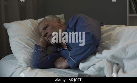 Grauhaariger Mann im Bett liegen und leiden unter Schlaflosigkeit, Depressionen und Gesundheit, Filmmaterial Stockfoto
