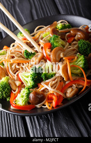 Gebratenen Soba Nudeln mit Champignons, Brokkoli, Möhren, Paprika closeup auf einem Teller auf dem Tisch. Vertikale Stockfoto