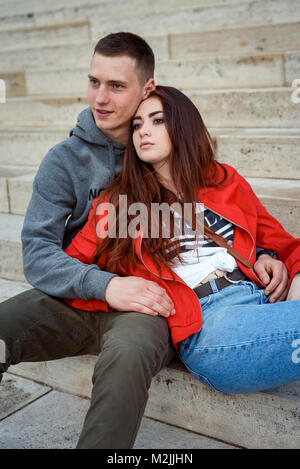 Close-up Portrait der charmante junge Paar in Liebe Hände halten und sitzt auf der Treppe des alten historischen Gebäude in Budapest, Ungarn. Den roten Kopf Mädchen ist, an ihren Geliebten gelehnt. Stockfoto