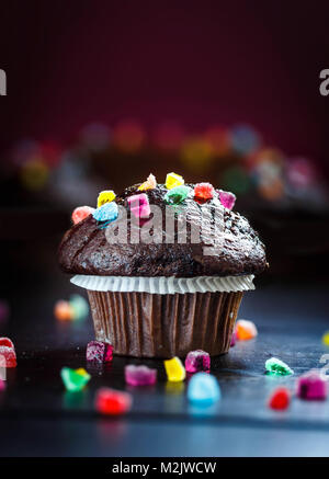 Lecker und lustig Chocolate Muffin mit Bonbons auf Holztisch mit bokeh Hintergrund. Selektive konzentrieren. Kopieren Sie Platz. Stockfoto