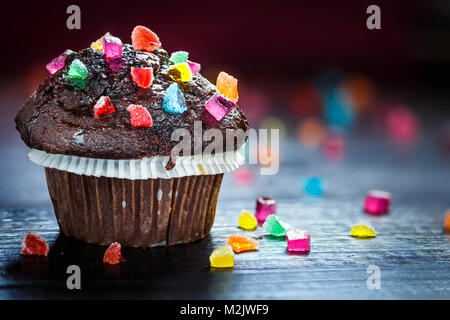 Lecker und lustig Chocolate Muffin mit Bonbons auf Holztisch mit bokeh Hintergrund. Selektive konzentrieren. Kopieren Sie Platz. Stockfoto