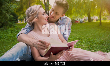 Glückliches Paar auf Teppich Buch sitzen und zärtlich an jedem anderen Suchen Stockfoto