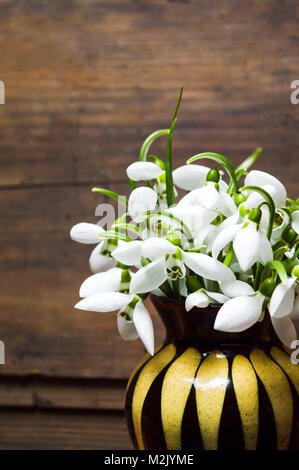 Snowdrop Blumen in einer Vase gegen rustikalen Holzmöbeln Hintergrund Stockfoto