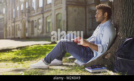 Männliche Studenten sitzen unter Baum, Buch lesen, Auswendiglernen Informationen Stockfoto