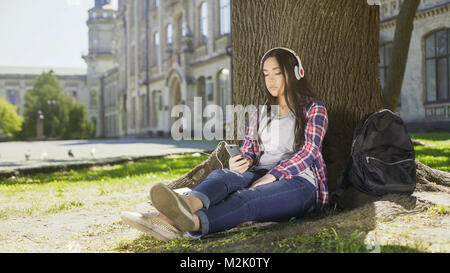 Multinationale Mädchen sitzen unter Baum im Kopfhörer, über das Telefon, Wahl song Stockfoto