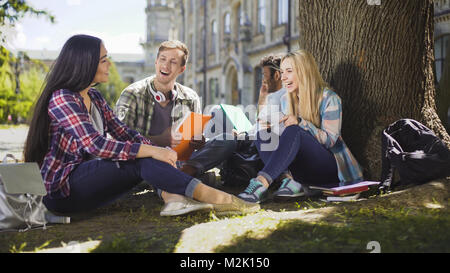 Gruppe von Freunden sitzen unter Bäumen, die miteinander sprechen, Lachen, miteinander Stockfoto