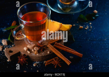 Doppelwand Glas Tasse mit heißem Tee und Zimt Zitrone auf einem dunklen Hintergrund. Gewürze für heiße Getränke. Gemütlich trinken Fotografie Konzept. Stockfoto