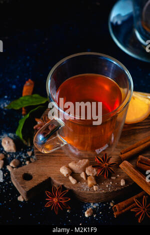 Doppelwand Glas Tasse mit heißem Tee und Zimt Zitrone auf einem dunklen Hintergrund. Gewürze für heiße Getränke. Gemütlich trinken Fotografie Konzept. Stockfoto