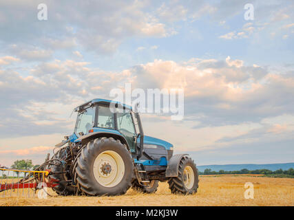 Eine blaue Traktor beherrscht eine vor kurzem Schnitt hayfield vor dem Hintergrund eines blauen Himmel und Wolken. Catoctin sind Berge in der Ferne. Stockfoto