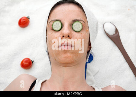 Weibliche Modell mit einer Tomate scrub aus frischen Tomaten, Kokosöl und Zucker mit Scheiben Gurke auf die Augen. Stockfoto