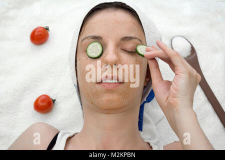 Weibliche Modell mit einer Tomate scrub aus frischen Tomaten, Kokosöl und Zucker mit Scheiben Gurke auf die Augen. Stockfoto