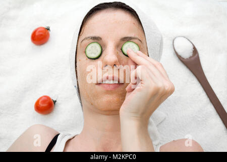 Weibliche Modell mit einer Tomate scrub aus frischen Tomaten, Kokosöl und Zucker mit Scheiben Gurke auf die Augen. Stockfoto